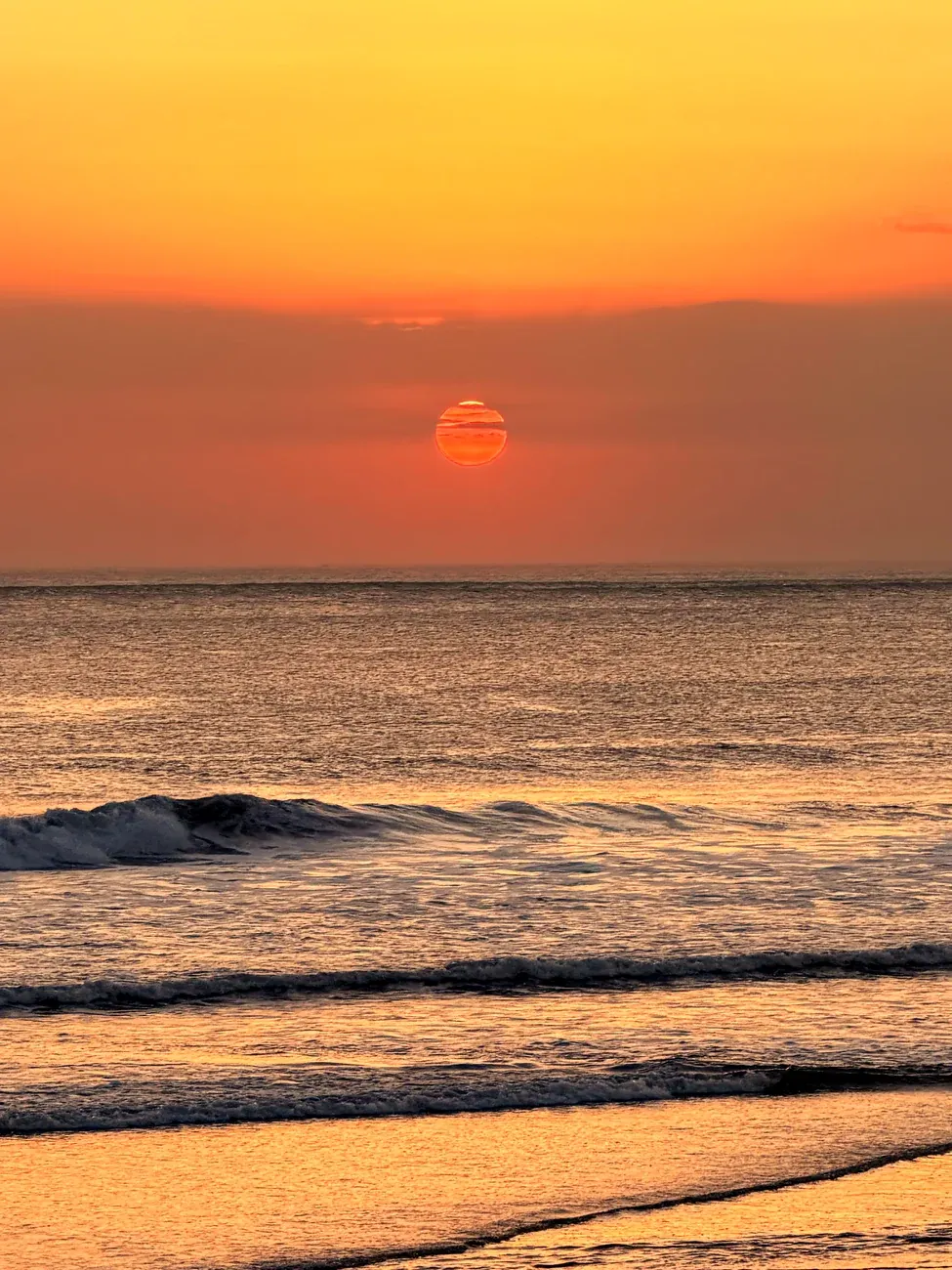 Eine rote Sonne über dem Meer, davor Wellen