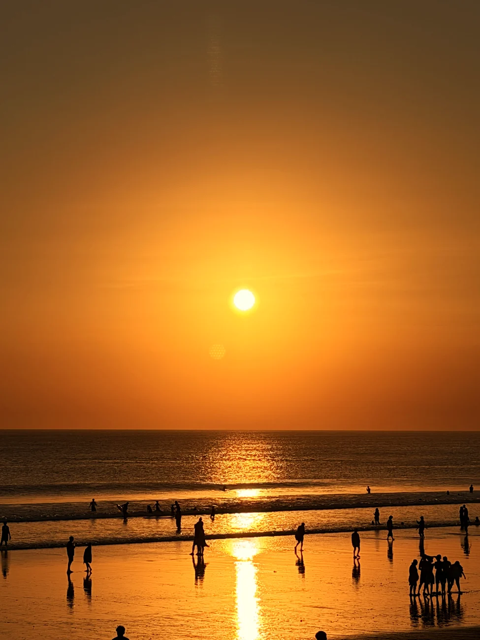 Die Sonne über dem Meer, davor Menschen am Wasser