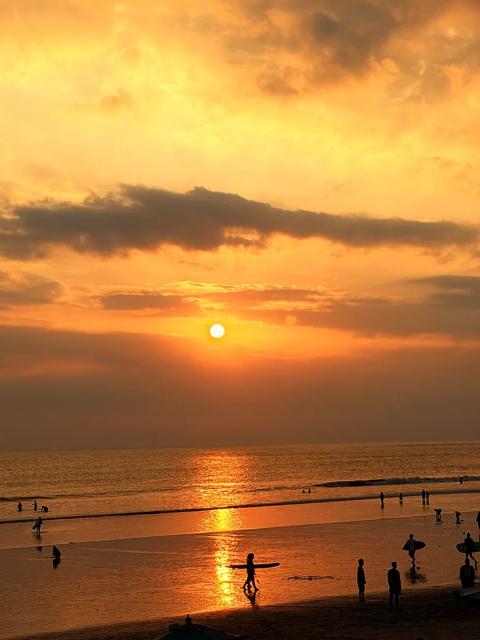 Surfer mit Brett im Gegenlicht vor dem orangefarbenen Himmel