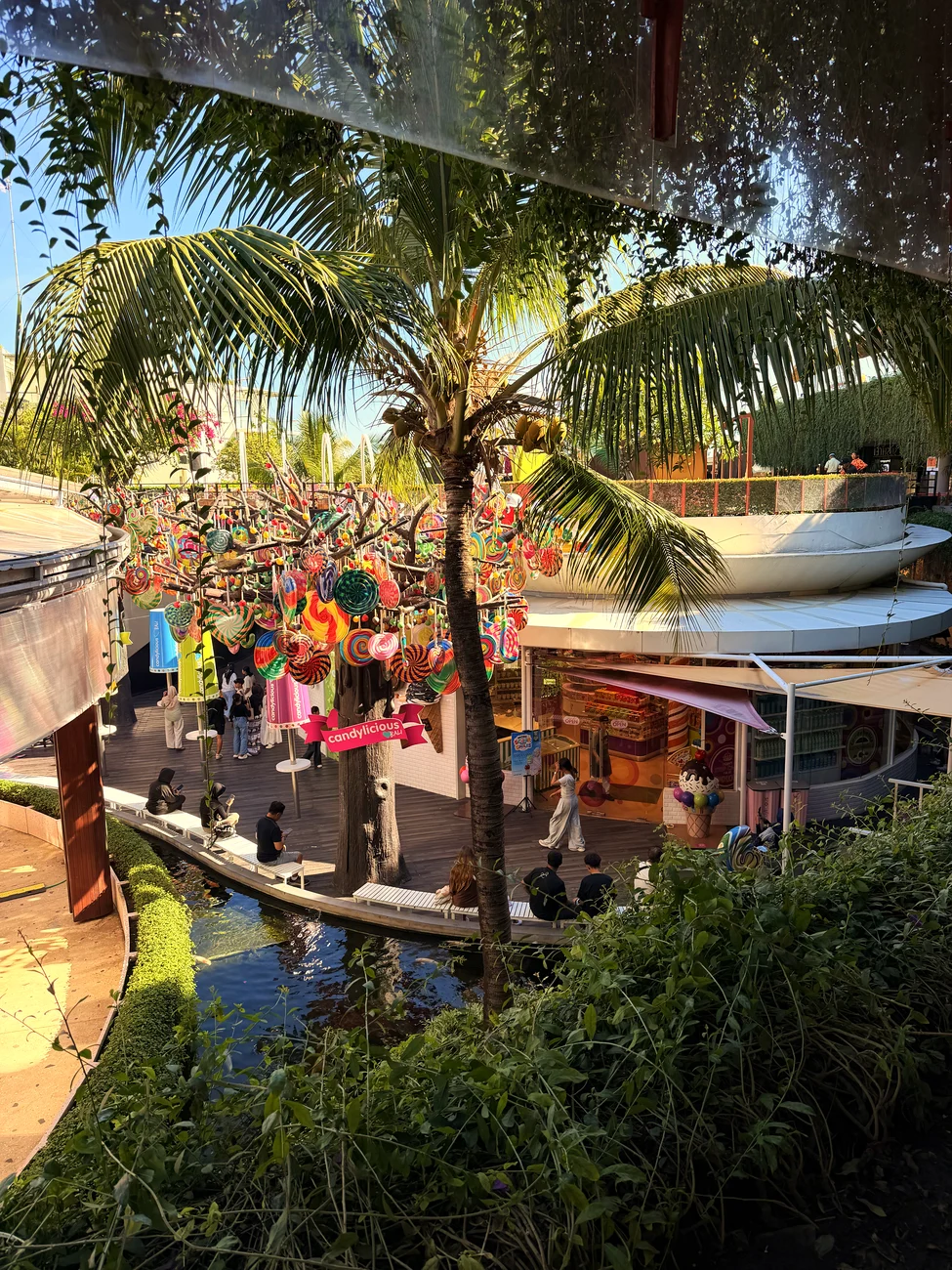 Der Garten des Einkaufszentrums Beachwalk mit Wasserlauf, Palmen und bunten Dekorationen.
