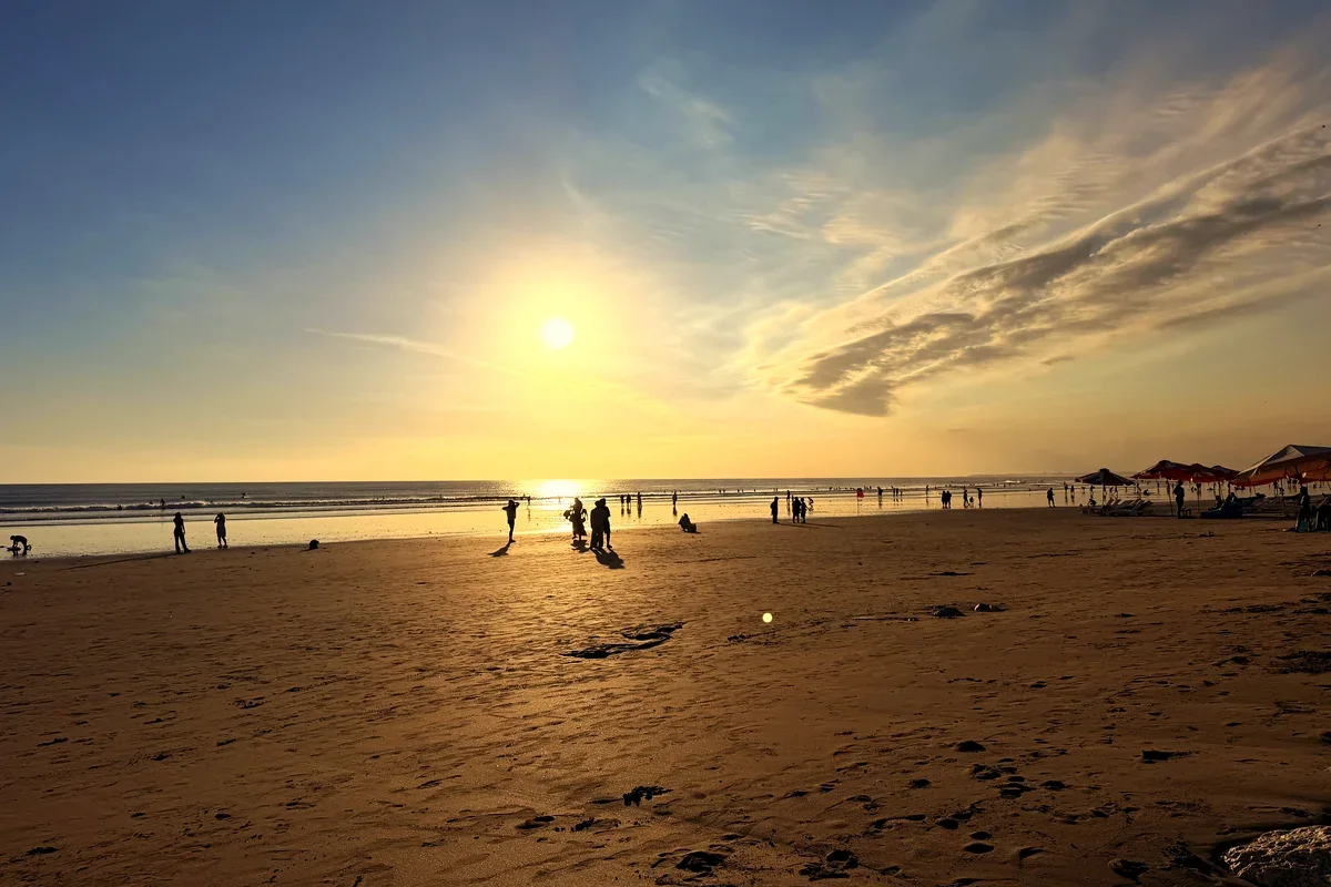 Sonne über dem Strand von Kuta auf Bali, im Vordergrund Sand und Felsen
