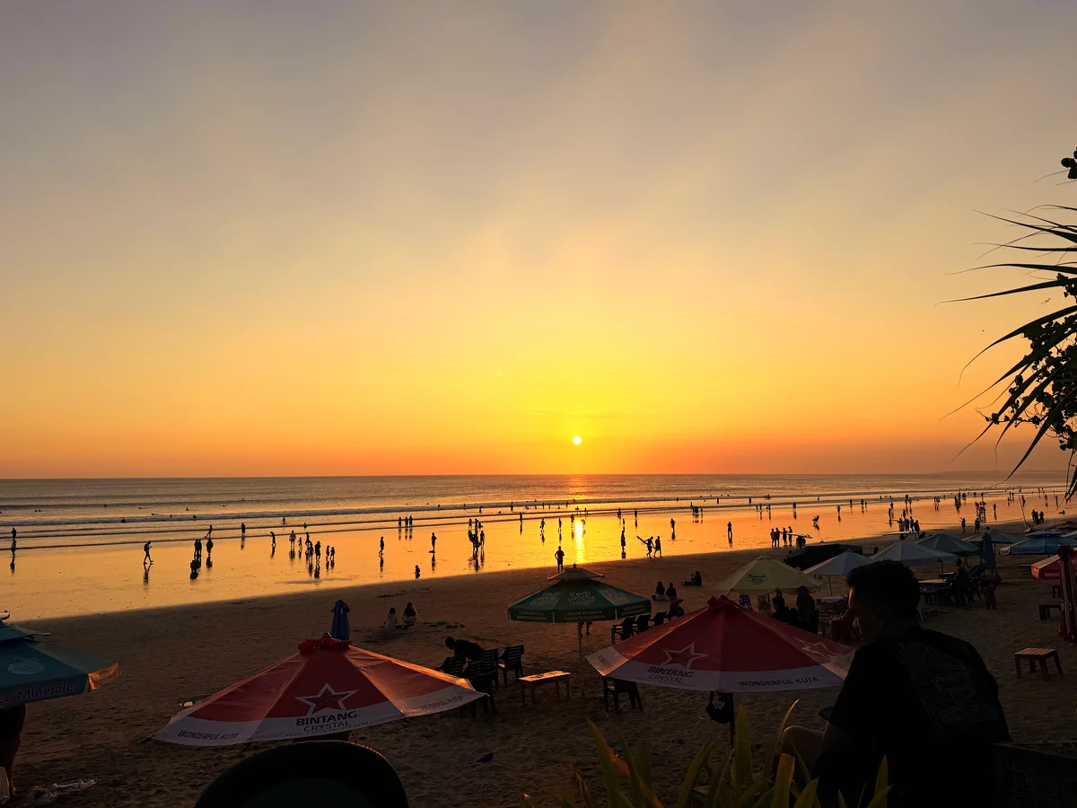 Orangefarbener Himmel über dem Meer, am Strand Sonnenschirme.