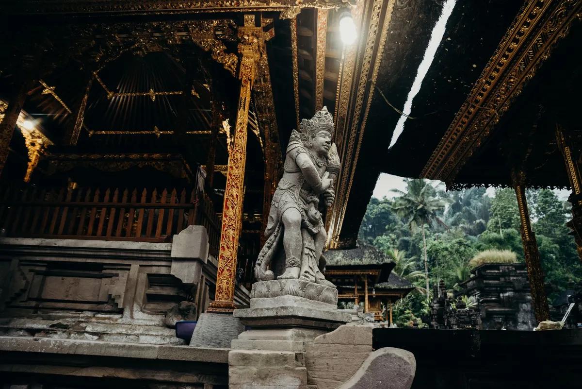 Steinerne Waechterfigur und goldverzierte Holzpavillons im Tirta-Empul-Tempel