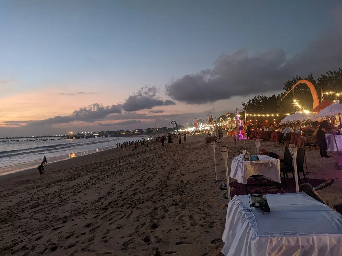 Strand von Jimbaran in der Dämmerung, gedeckte Tische im Sand und Lichterketten