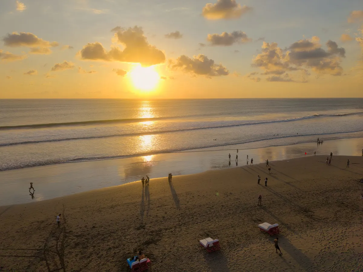 Sonnenuntergang am Strand von Seminyak mit Spaziergaengern auf goldenem Sand