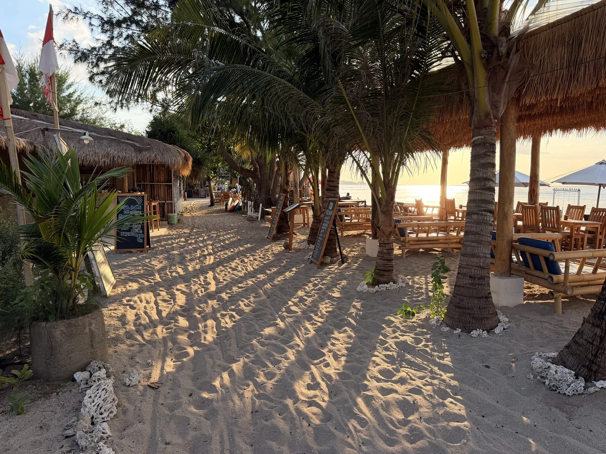 Sandweg mit Palmen und Warungs an der Ostküste von Gili Air