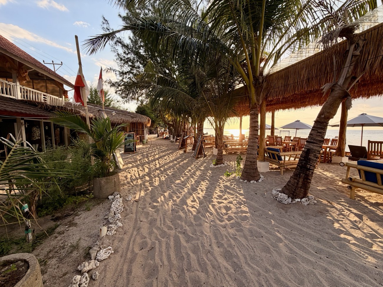 Sandweg am Strand von Gili Air, gesäumt von Palmen und kleinen Restaurants