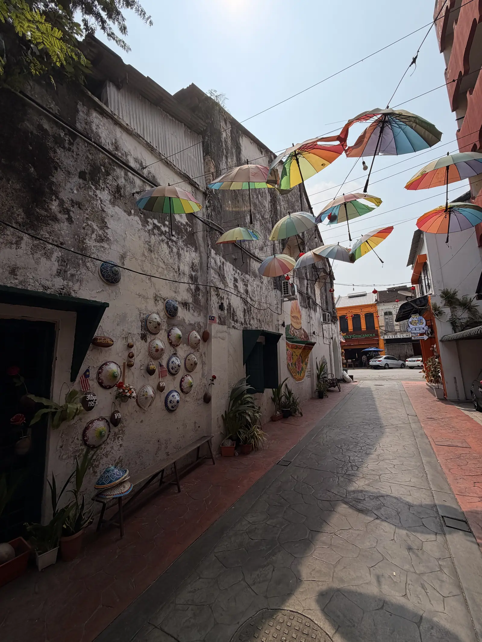 Die Market Lane mit Regenschirmen in der Luft und Strohhüten an der Wand