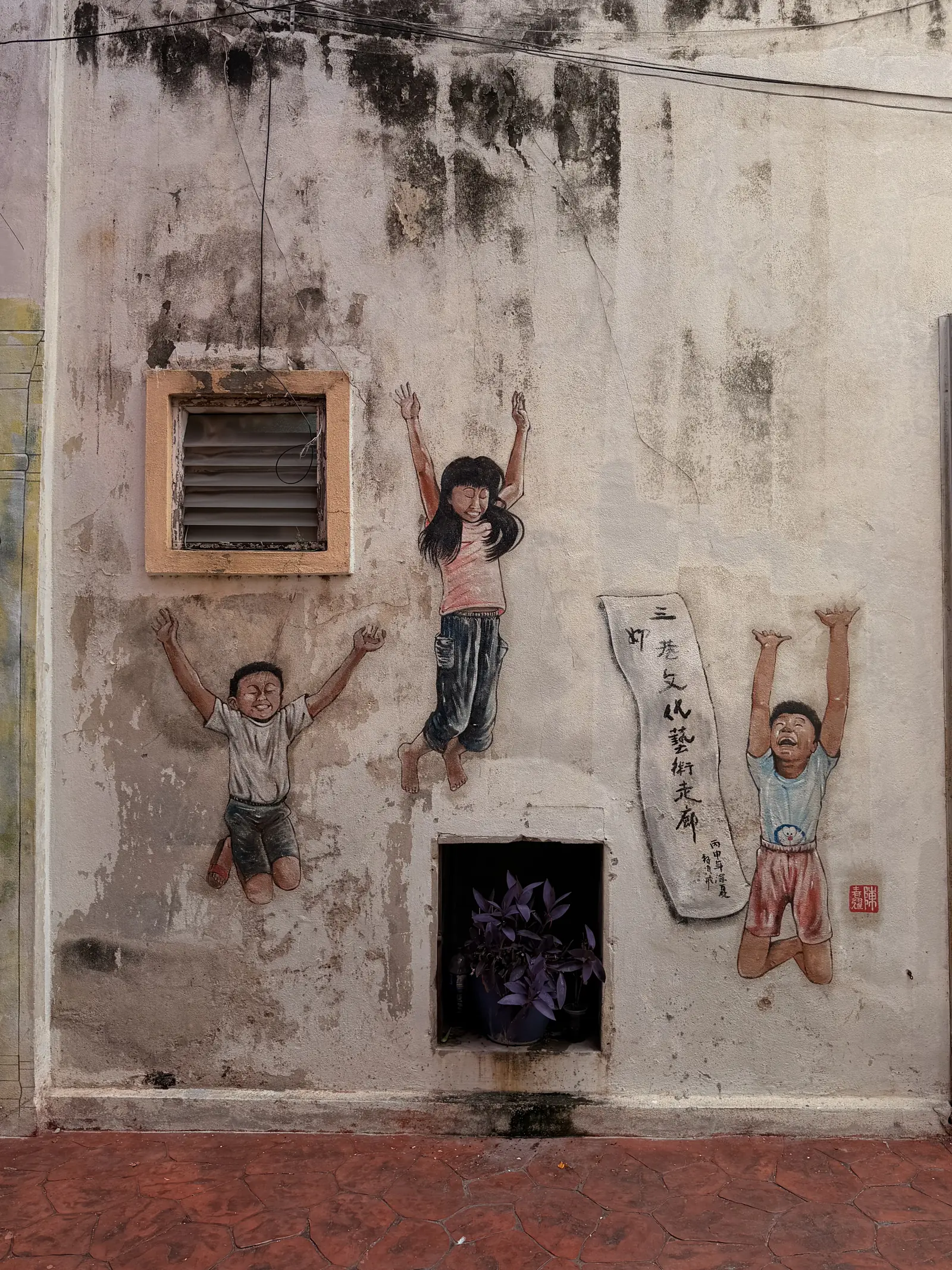 Wandbild von zwei Kindern, die mit erhobenen Armen an einer alten Hauswand hängen