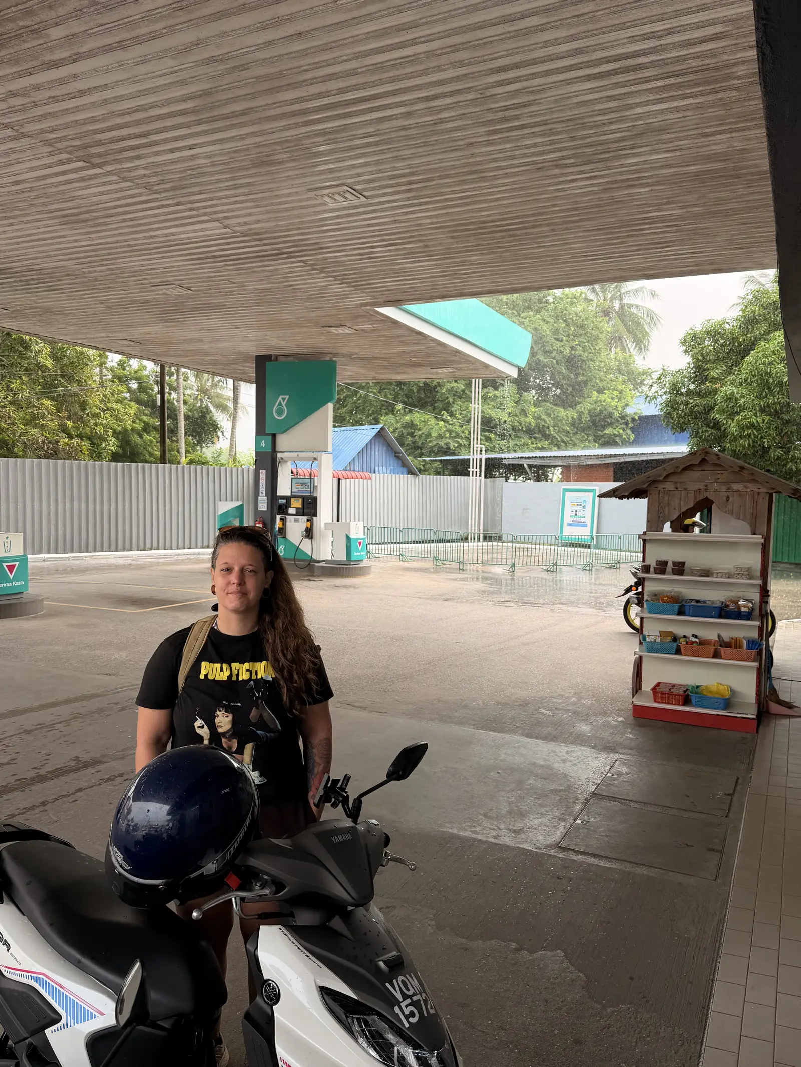 Fabienne auf dem Roller unter dem Dach einer Tankstelle im Regen