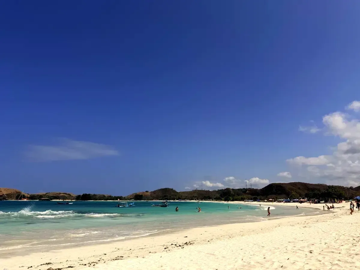 Weisser Strand mit flachen Wellen und Hügeln im Hintergrund