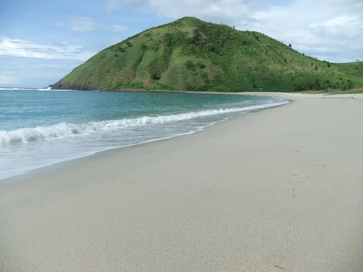 Langer heller Strand von Mawun mit grünem Hügel