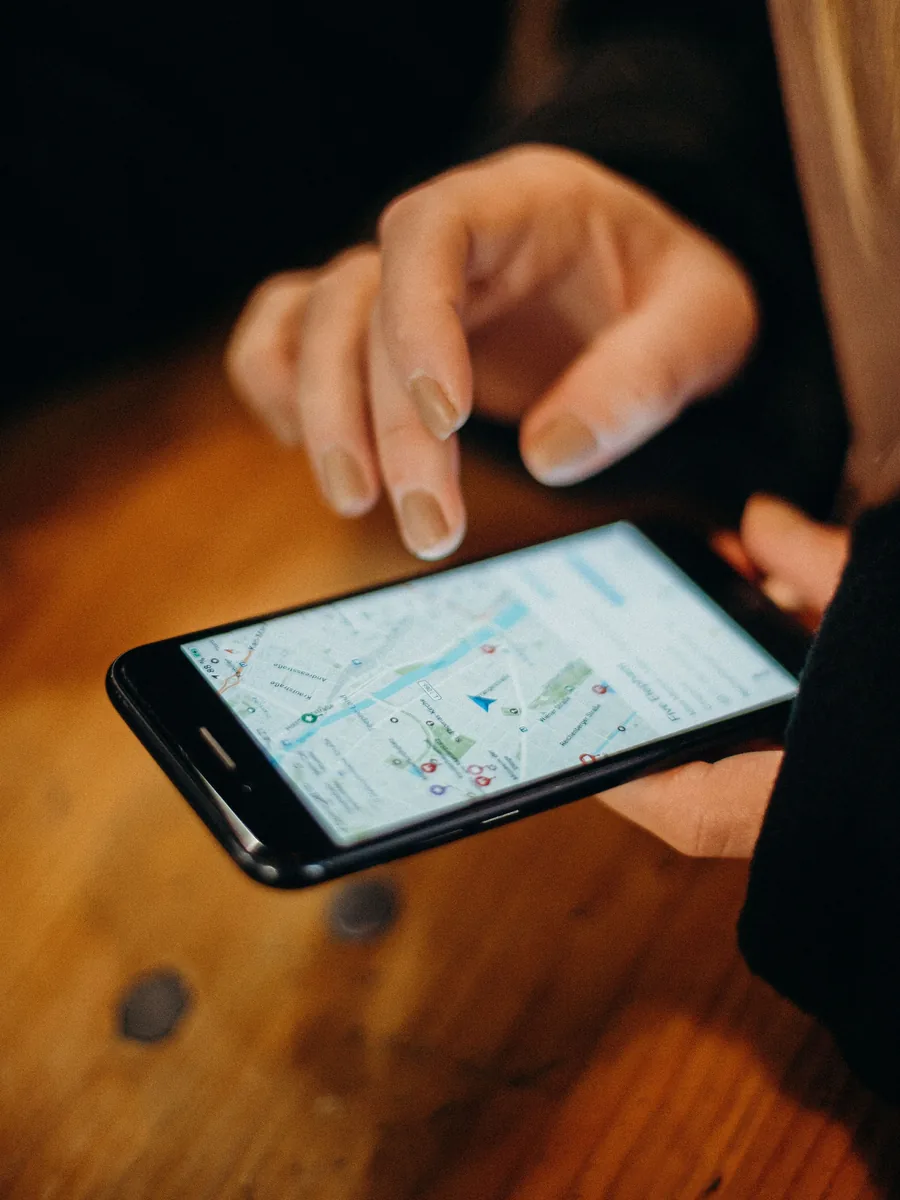 Hand tippt auf eine Karten-App auf dem Handy, über einem Holztisch